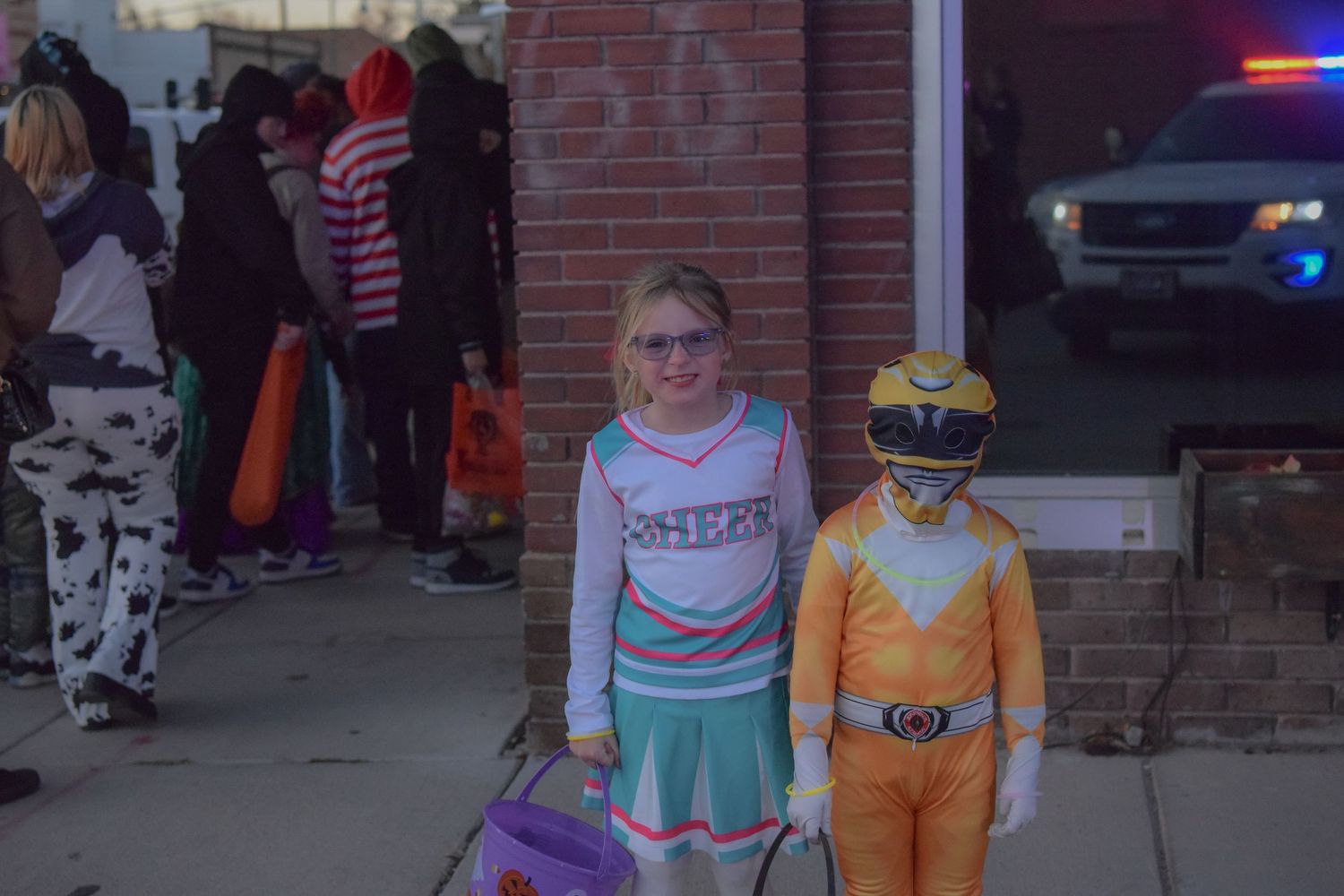 Children in costumes line up outside a building during a Halloween trick-or-treat event.