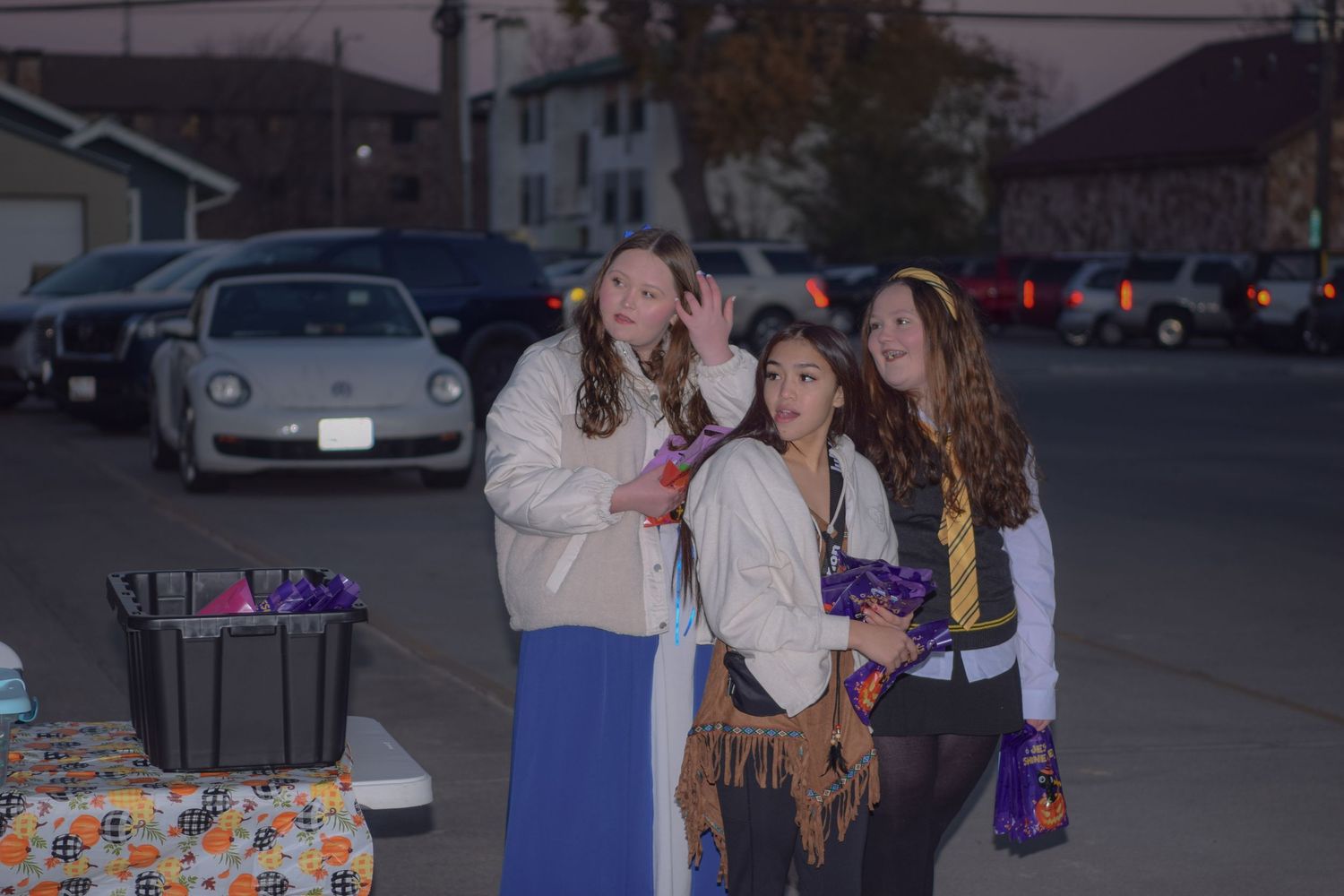 People collecting treats at a nighttime Halloween event outside brick buildings.