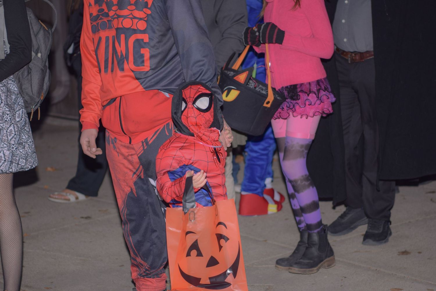 Children in Halloween costumes waiting in line for candy at night.