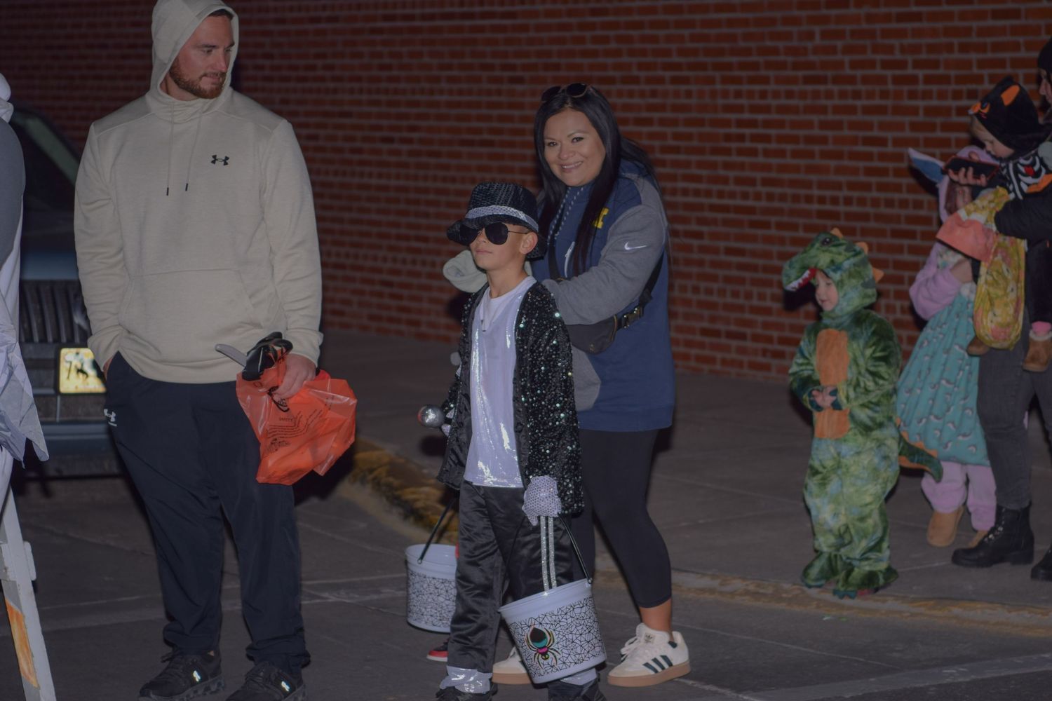 Families lined up along a brick wall during an evening Halloween celebration.