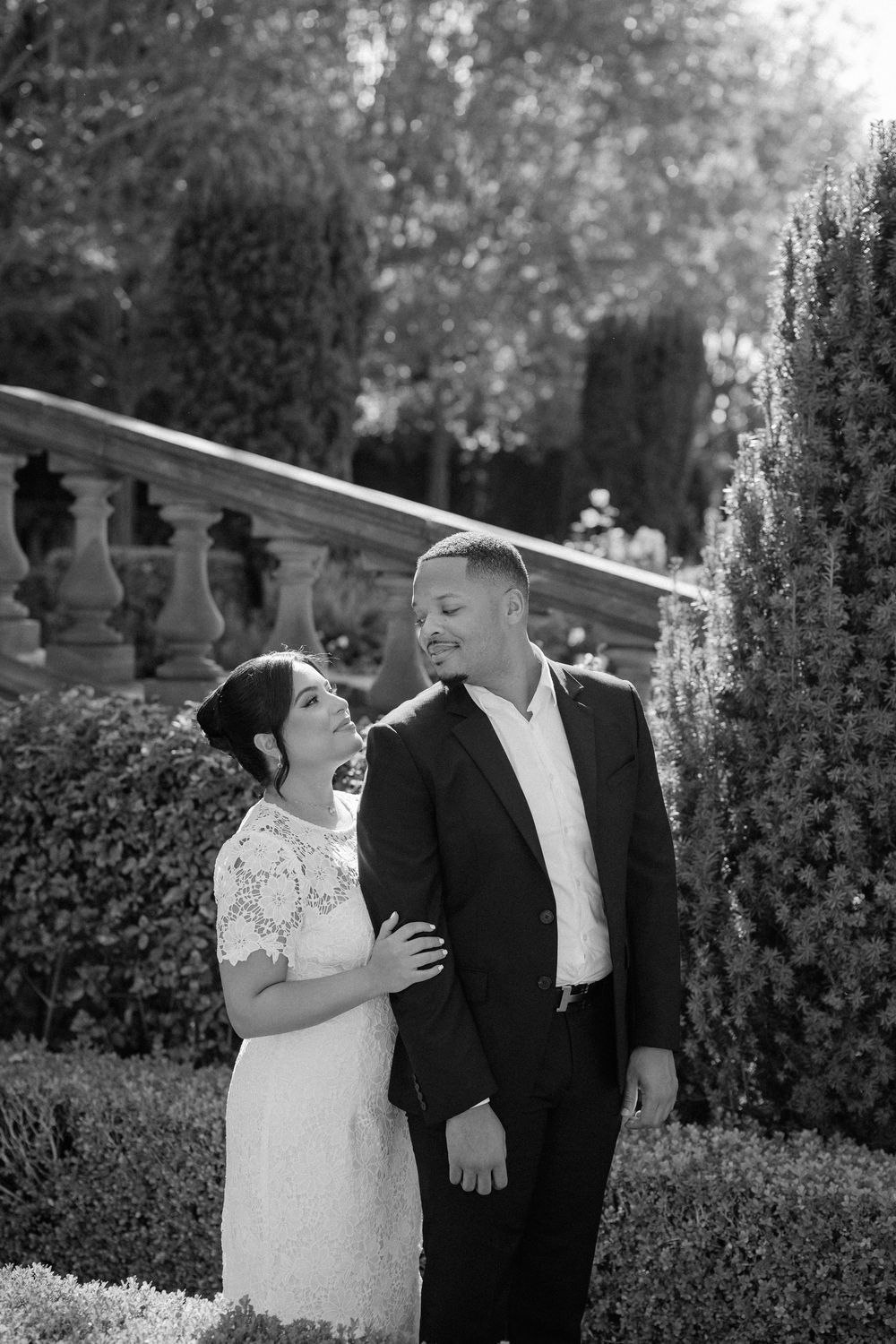 A couple shares candid laughter together in a garden setting during a wedding photoshoot.