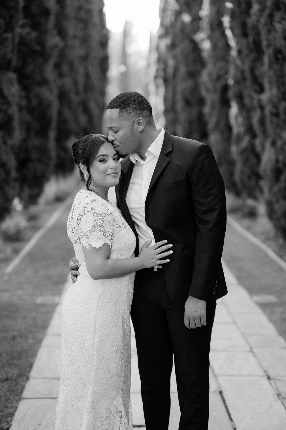 Black and white wedding photos of couple embracing on tree-lined path in romantic outdoor setting.