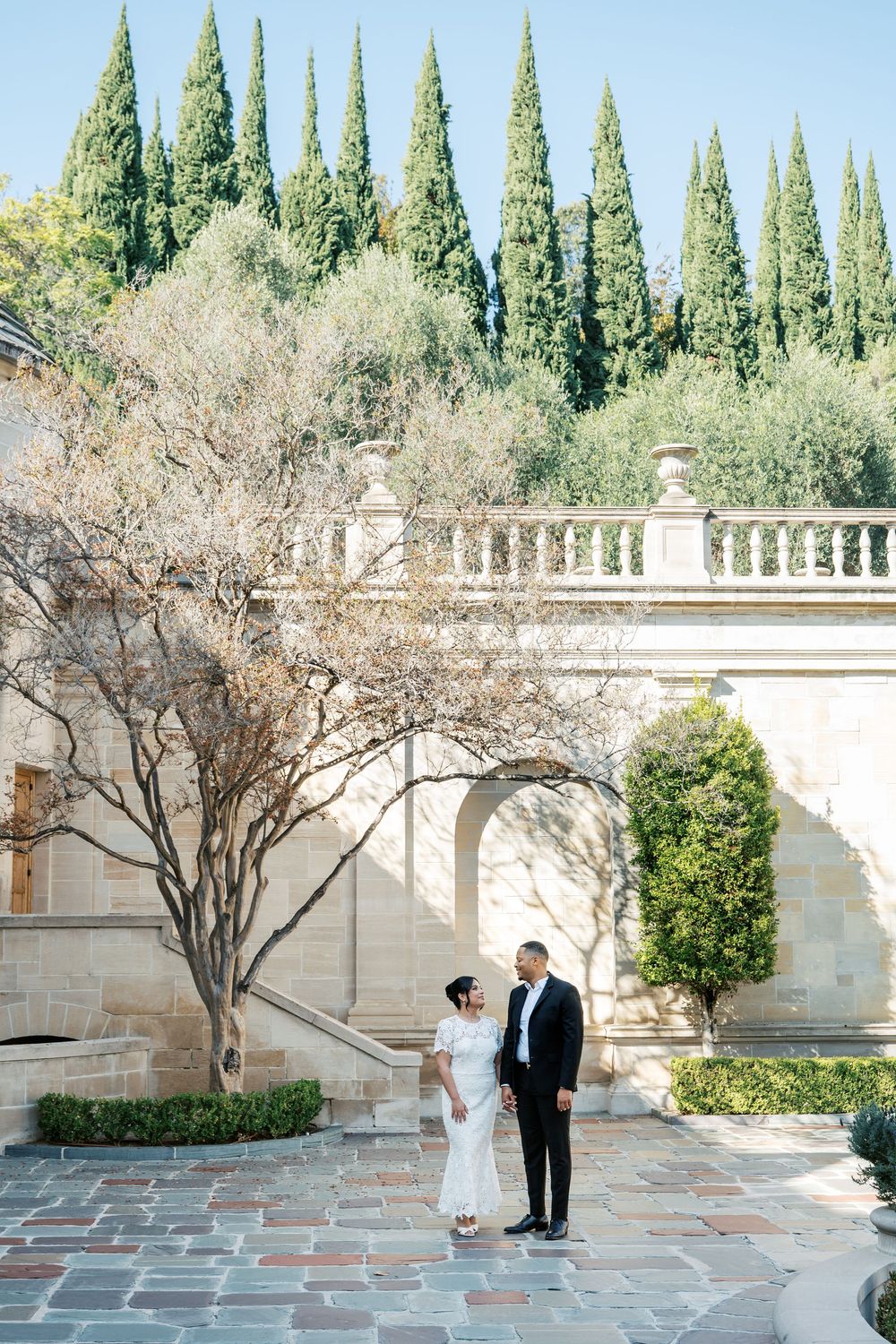 A romantic courtyard scene with cypress trees and stone balustrades at an elegant venue during a wedding ceremony.