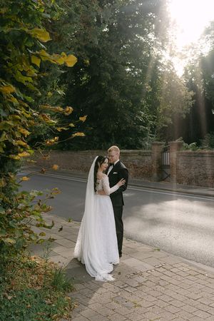 Newlyweds dancing together on a sunlit stone path surrounded by autumn trees.