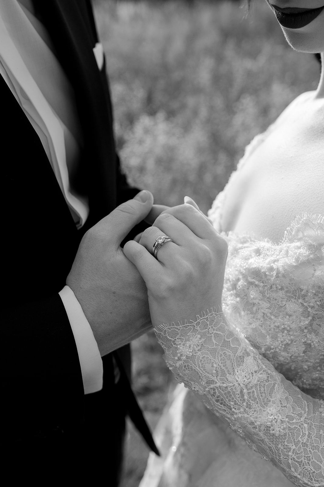 Intimate black and white close-ups of wedding couple's hands with lace dress details.