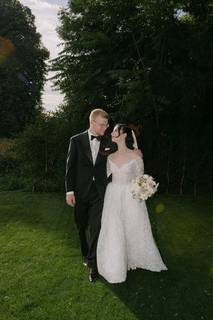 Wedding couple walking together through a lush green garden path in formal attire.