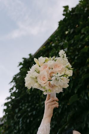 A hand holds up a delicate bouquet of pale pink and white flowers against a dark leafy background.