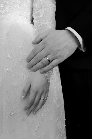 Close-up of hands wearing wedding rings against white lace fabric.