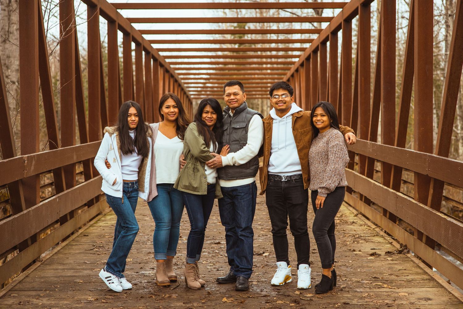 A group stands together smiling on a wooden bridge with rustic metal beams overhead during autumn.