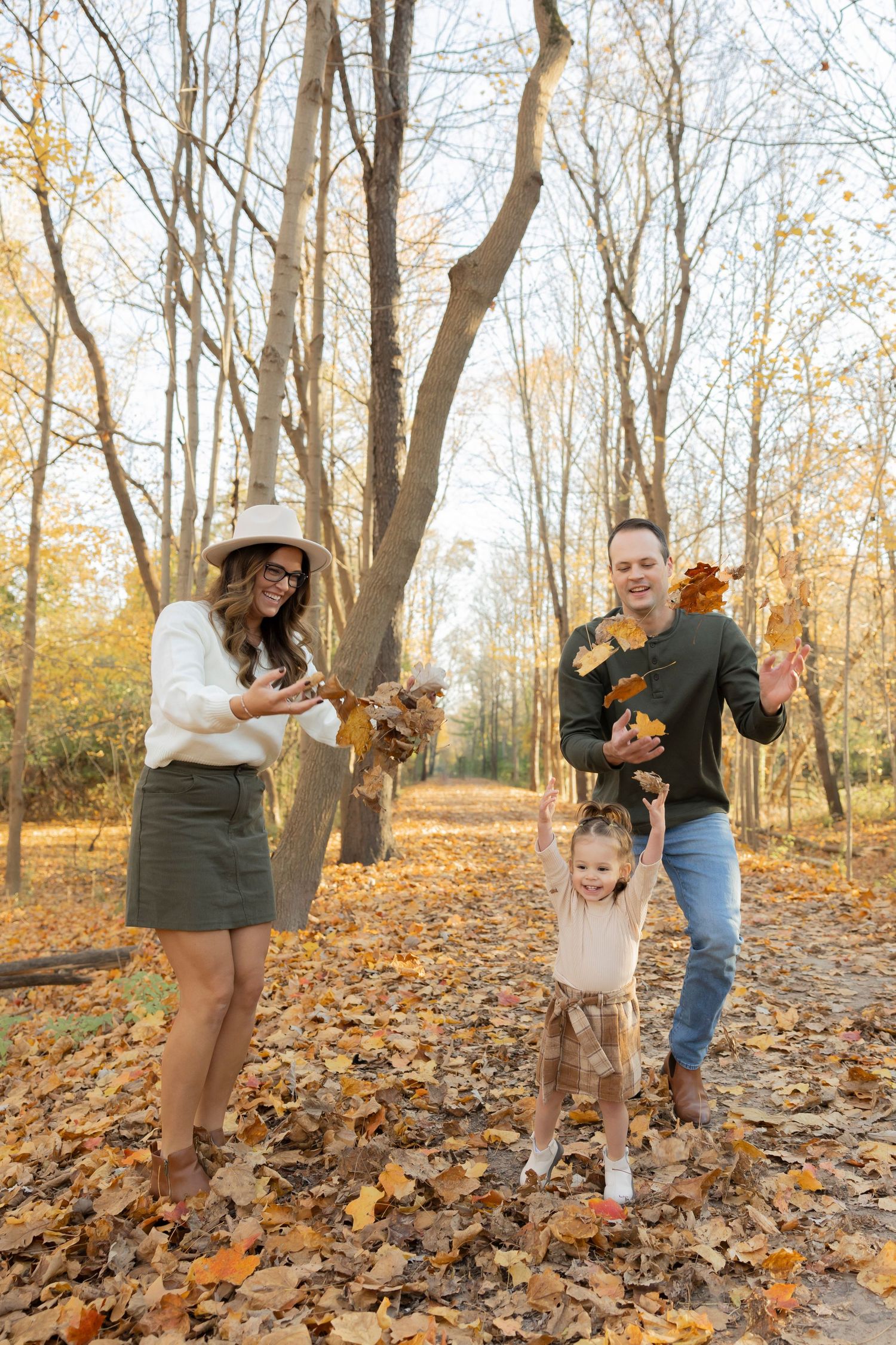 Family enjoying autumn day on the paint creek trail throwing leaves and playing together in fallen foliage in Rochester michigan