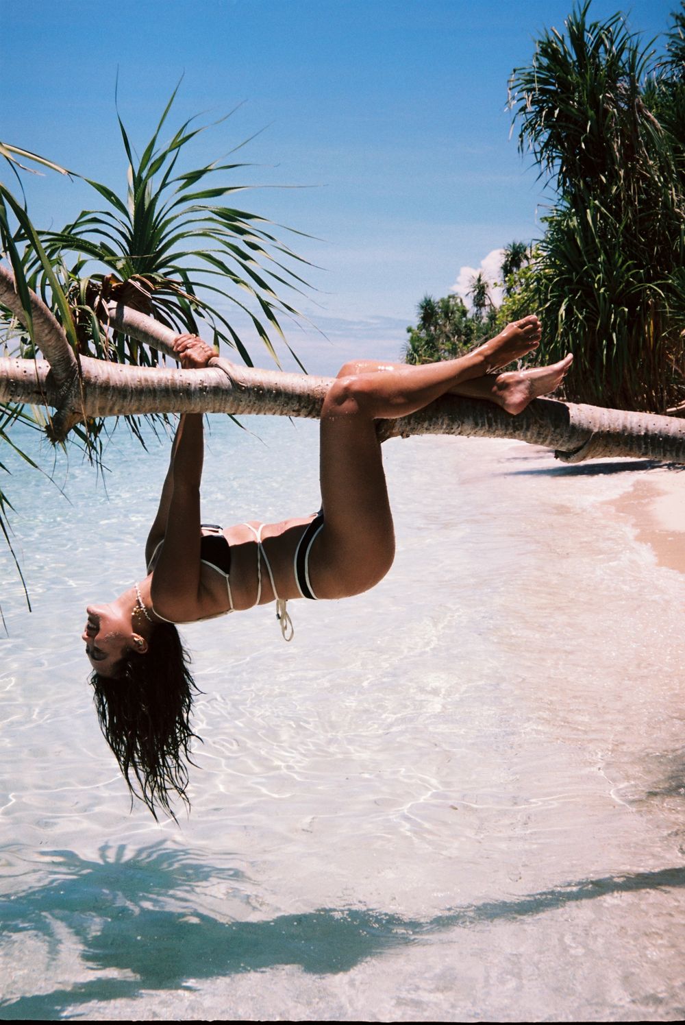Person floating and relaxing in shallow crystal clear waters near palm trees.