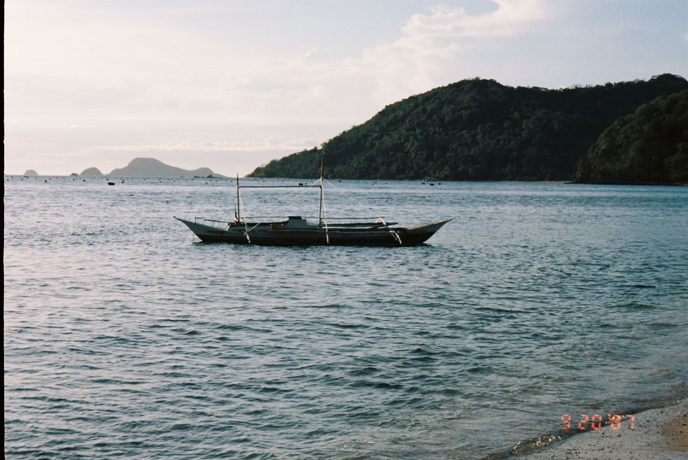 Scenic ocean view with traditional boats and mountainous islands in the distance.