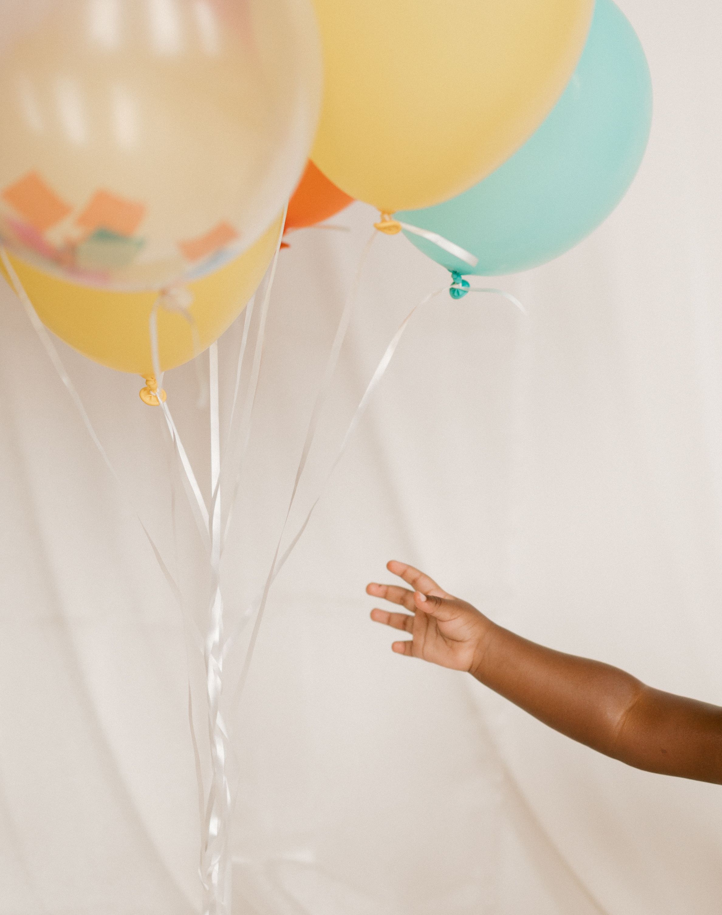 Colorful pastel balloons floating against a white background with a person's arm reaching towards them.