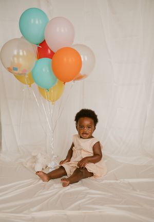 Happy toddler surrounded by pastel balloons plays on white fabric during a photo session.