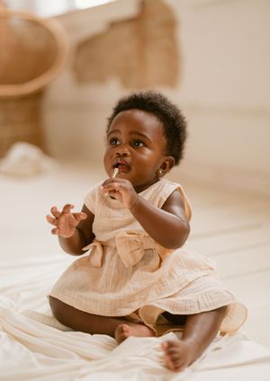 Series of candid shots showing baby in peach dress during first birthday photo session on white background.