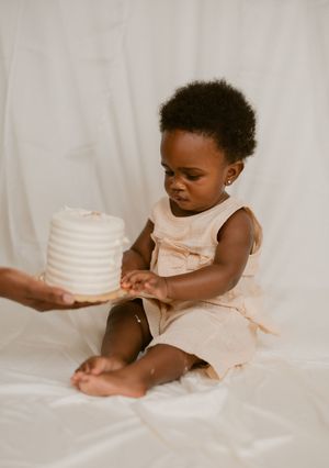 A series of images showing a small child in a white dress reaching for and playing with a white tiered cake.