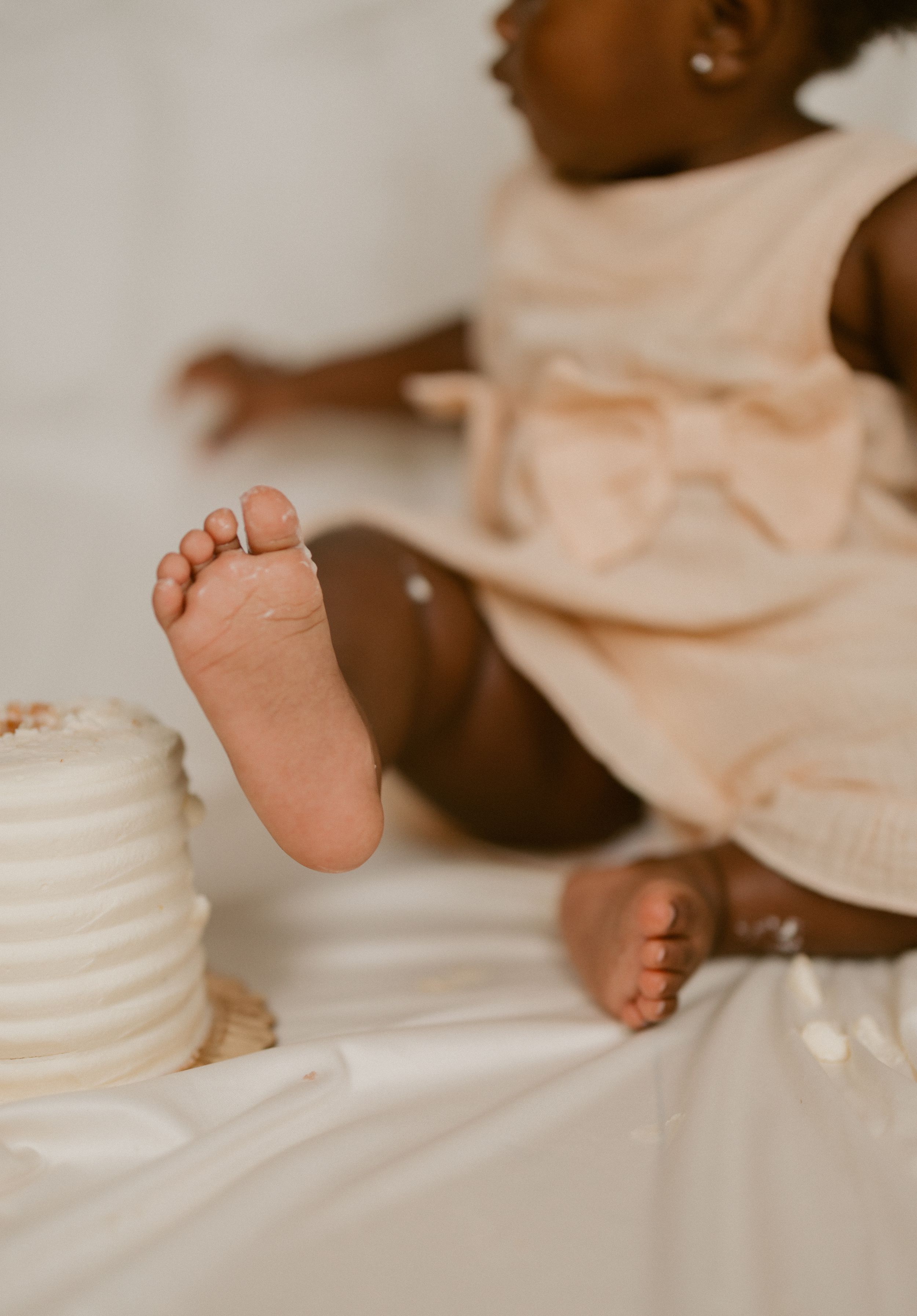 Close-up view of tiny baby feet against soft white bedding with peach-colored fabric visible.