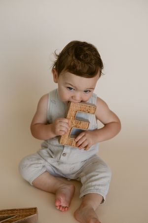 Baby in gray romper sits on beige floor playing with wooden blocks.