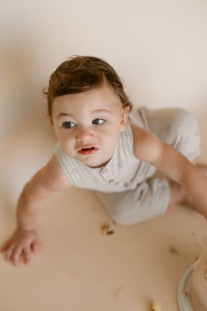 A small child in a white shirt lays on a beige surface while looking playfully to the side.