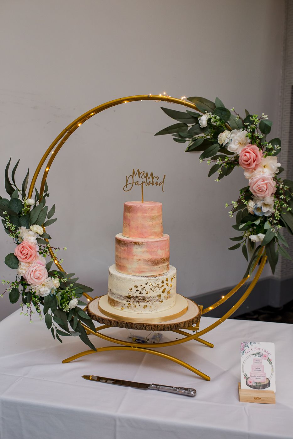 Wedding cake display featuring pink ombre design with gold accents and fresh roses.