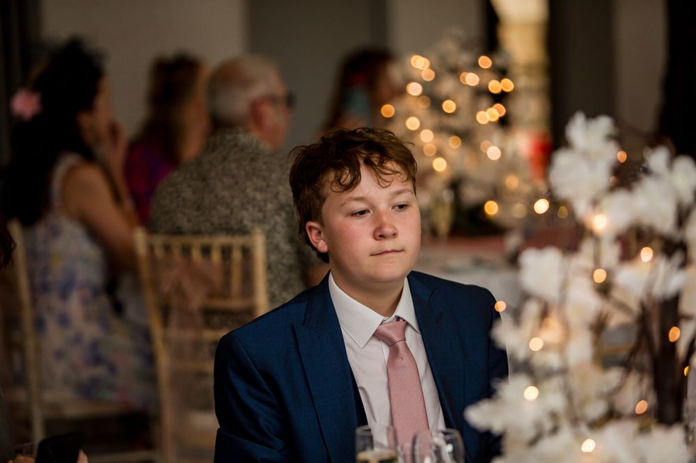 Wedding guests seated at elegant tables with twinkle light backdrop and floral centerpieces.