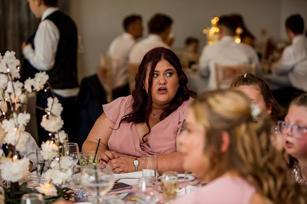 Wedding reception guests seated at decorated tables with pink and white floral arrangements.