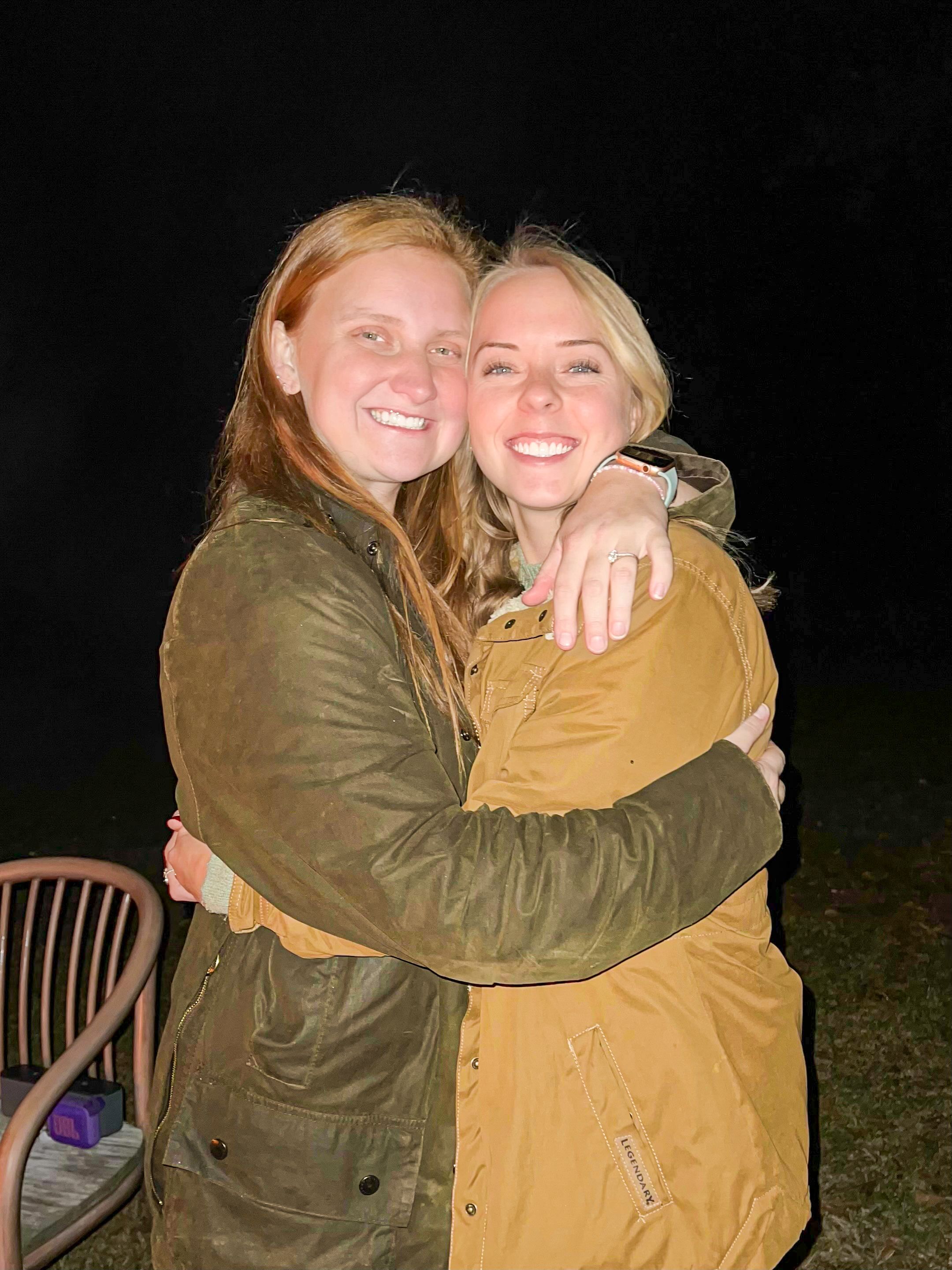 Two friends share a warm embrace while wearing casual jackets outdoors at night.