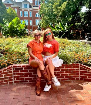 Two friends in bright orange outfits sitting together on a decorative brick wall.