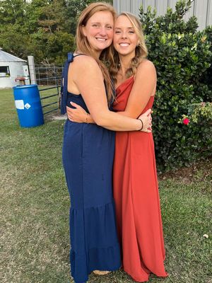 Two people in contrasting blue and coral dresses embrace while standing in a garden setting.