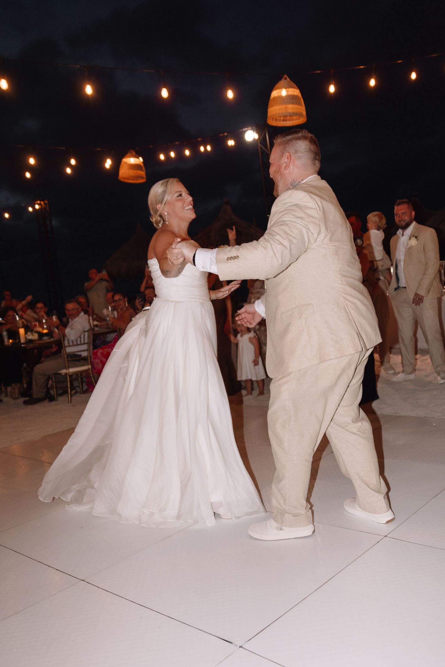 Wedding reception dance under string lights with couple dancing on white dance floor.