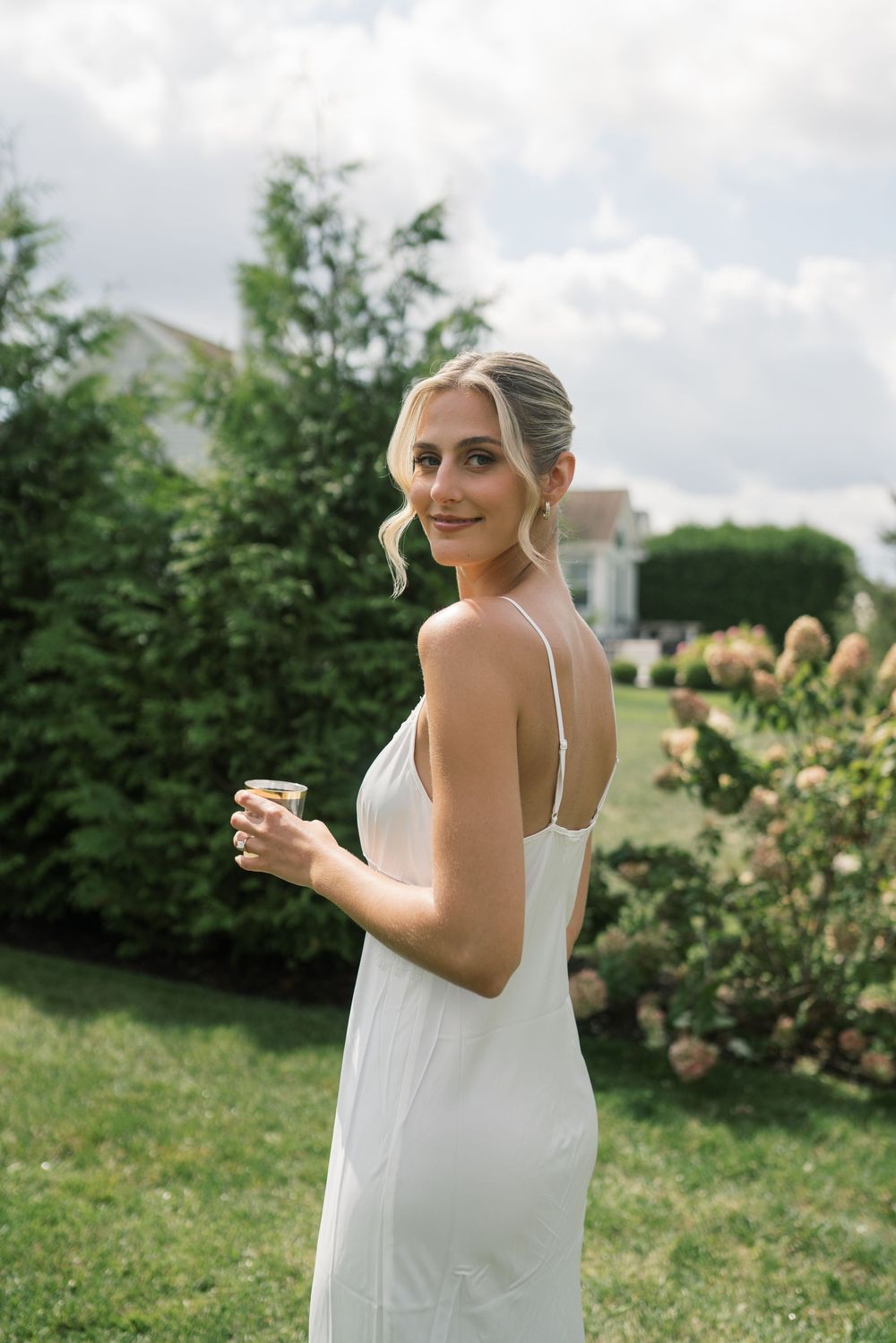 Woman in white dress enjoying a drink in an outdoor garden setting.