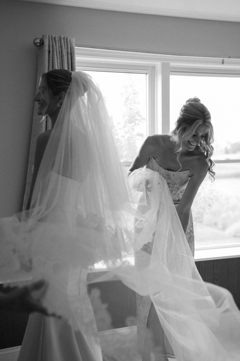 Black and white photo of wedding dress preparation with flowing veil movement.