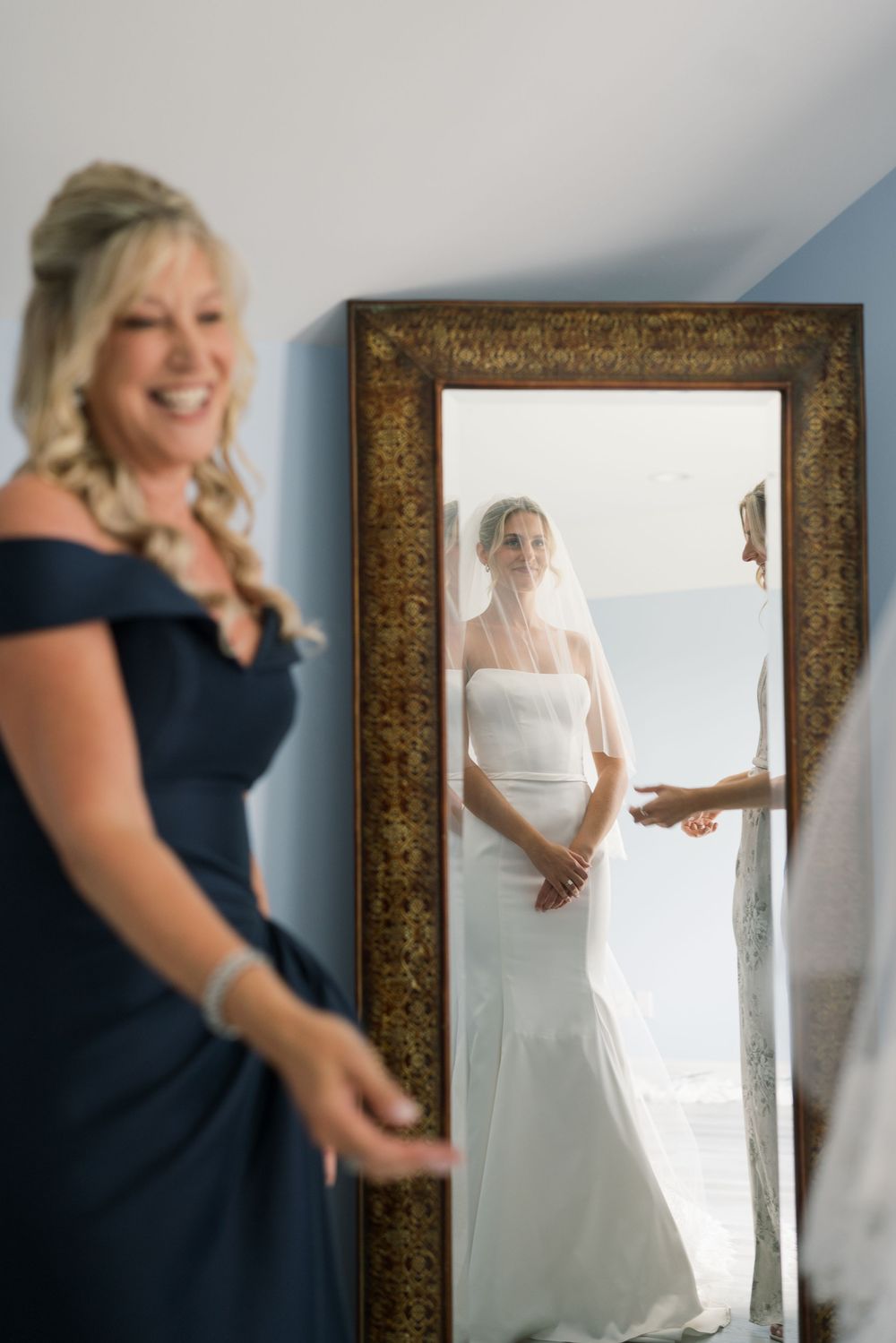 Wedding dress reflection in ornate gold mirror with navy bridesmaid dress in foreground.