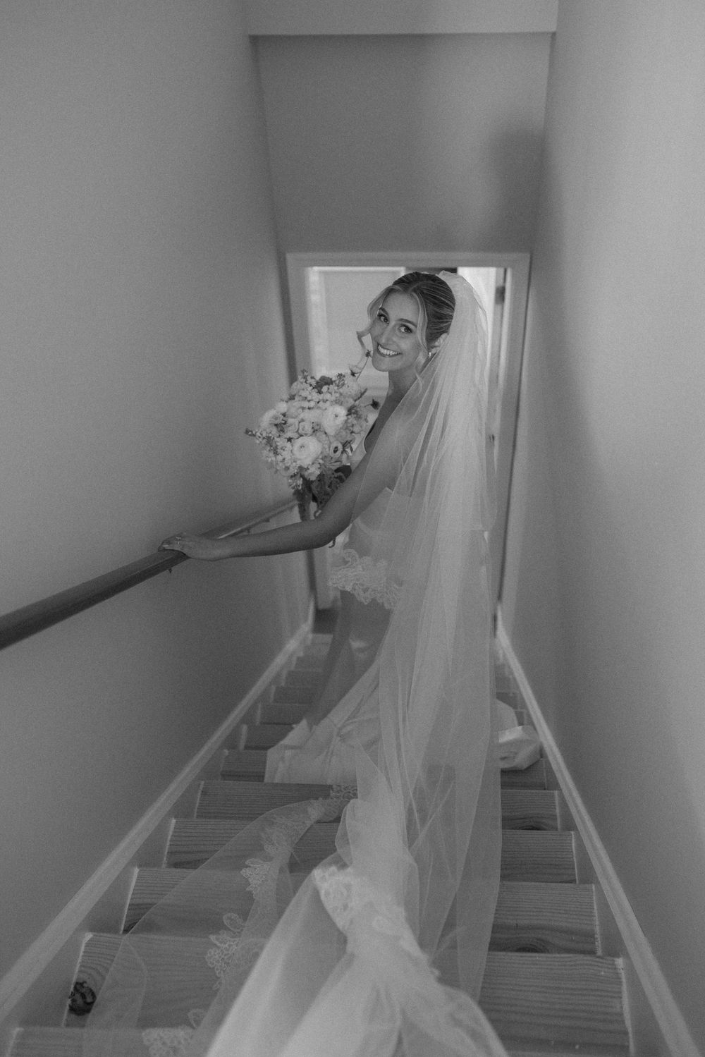 Wedding dress with flowing train photographed on staircase in black and white.