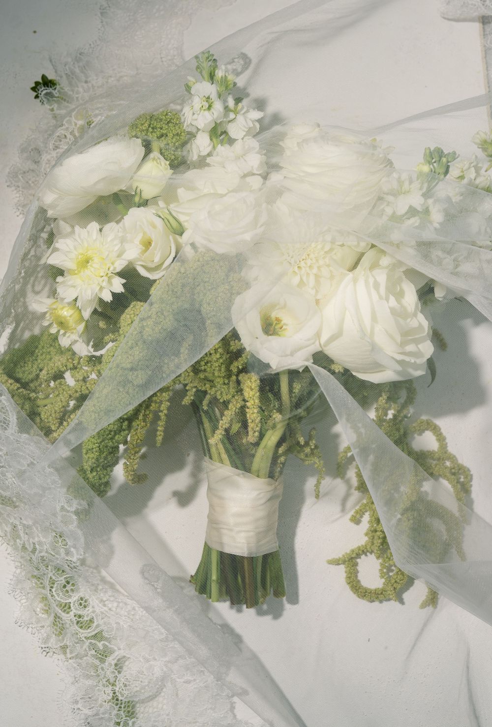 Delicate white wedding bouquet with roses and greenery on lace fabric.