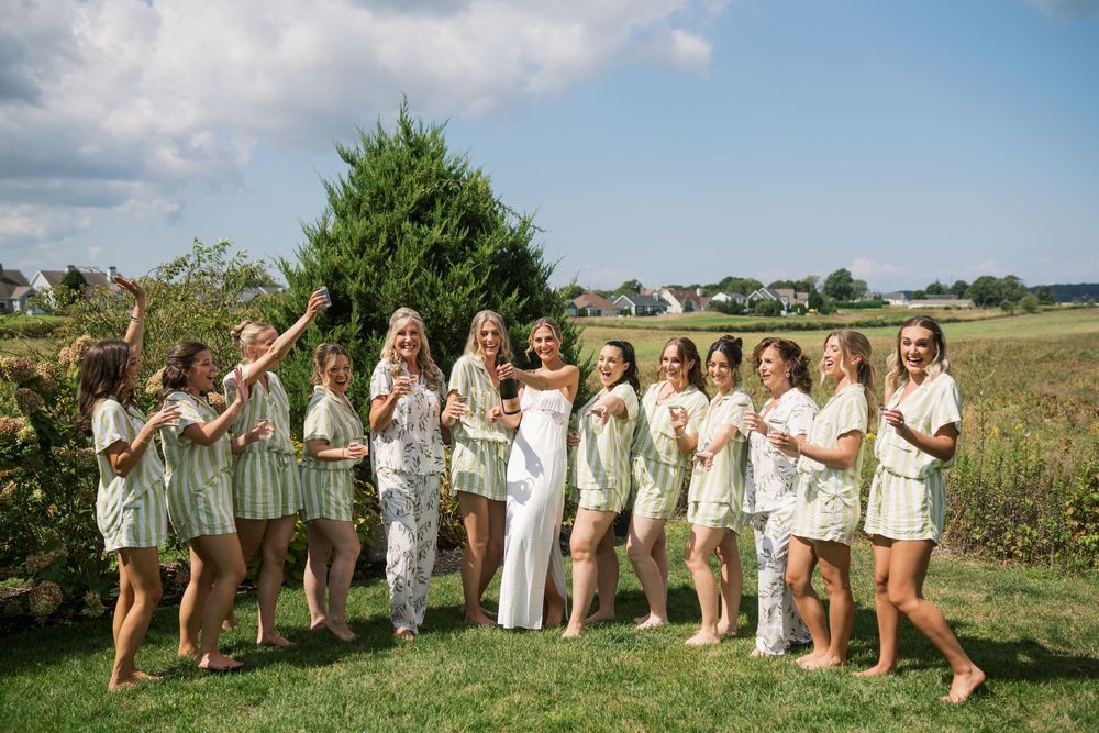 Group photo of wedding party in light-colored dresses outdoors.