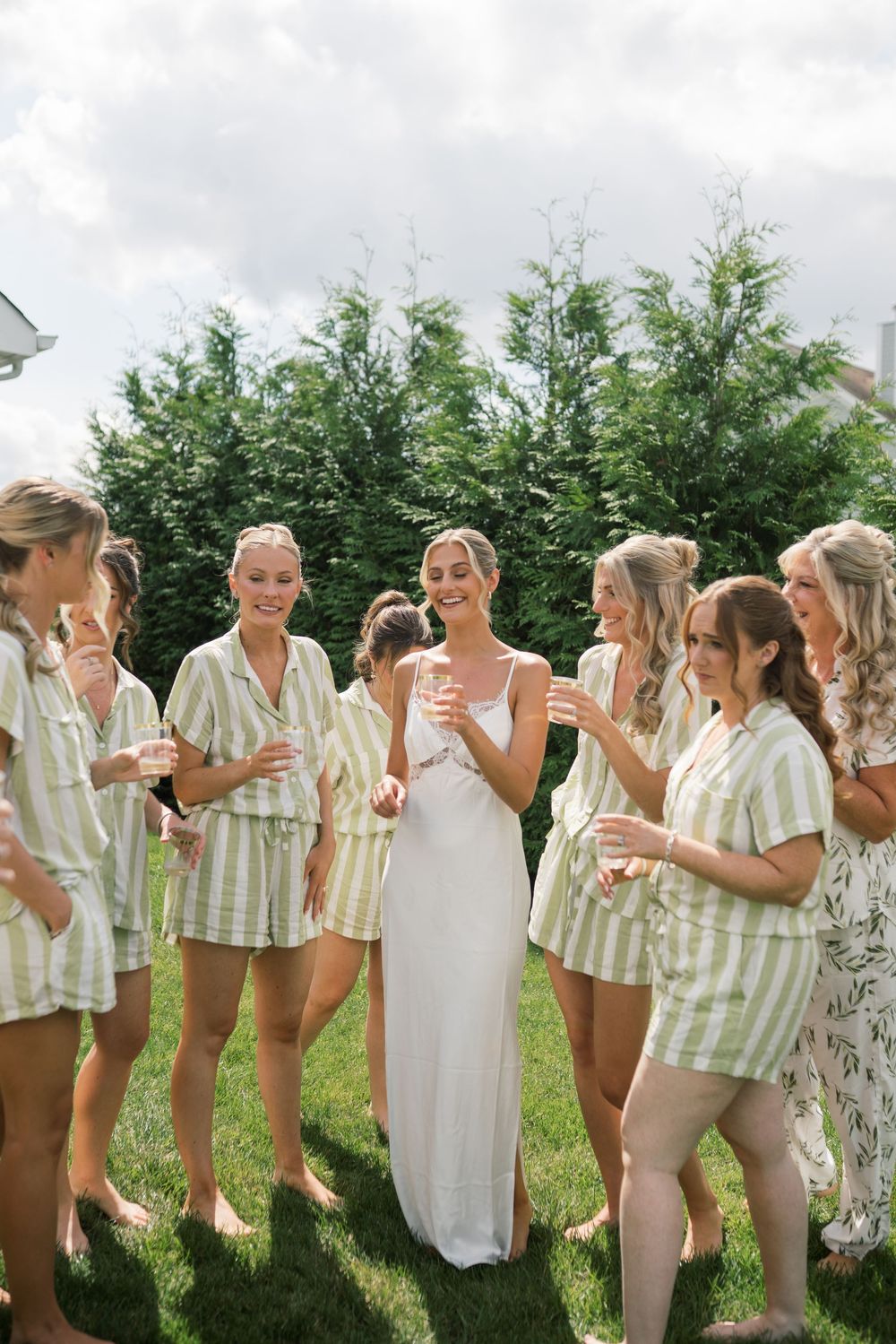 Wedding party in striped outfits and white dresses gathered on grass.