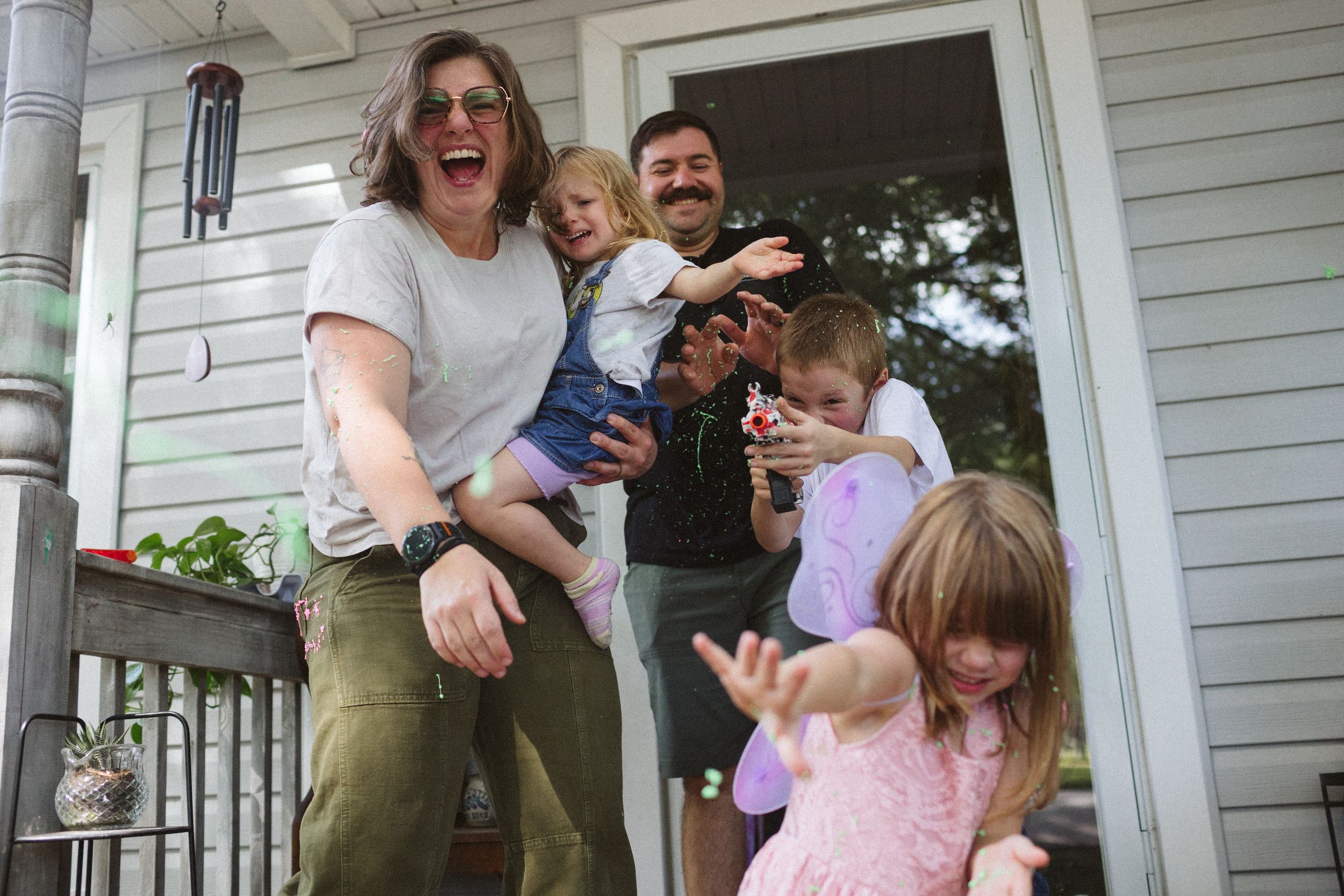 family laughs and celebrates on a white porch during a festive military homecoming with a silly string battle in the front yard. norfolk, va