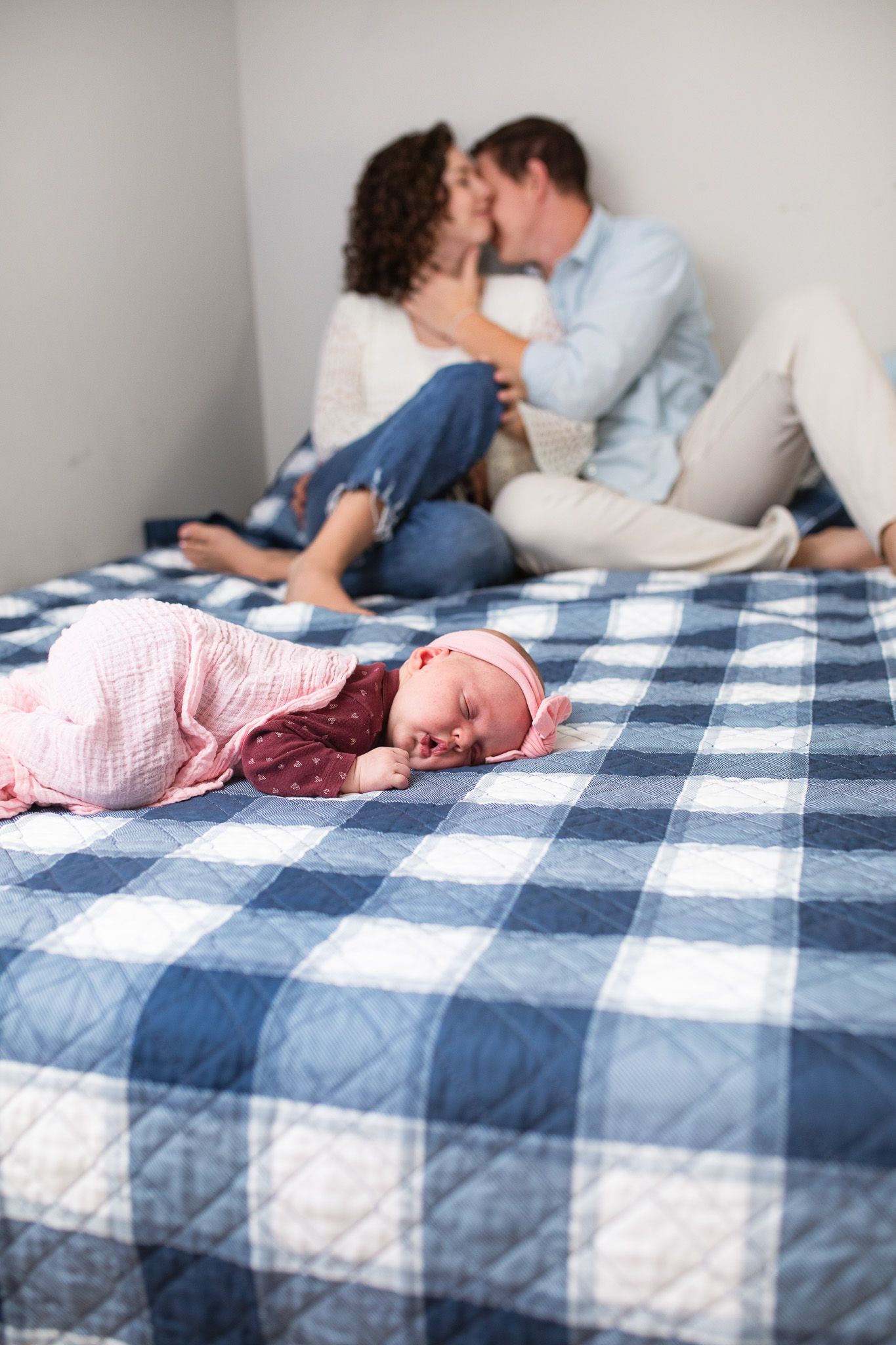 A sleeping newborn baby on a blue and white checkered blanket with a couple snuggled nearby