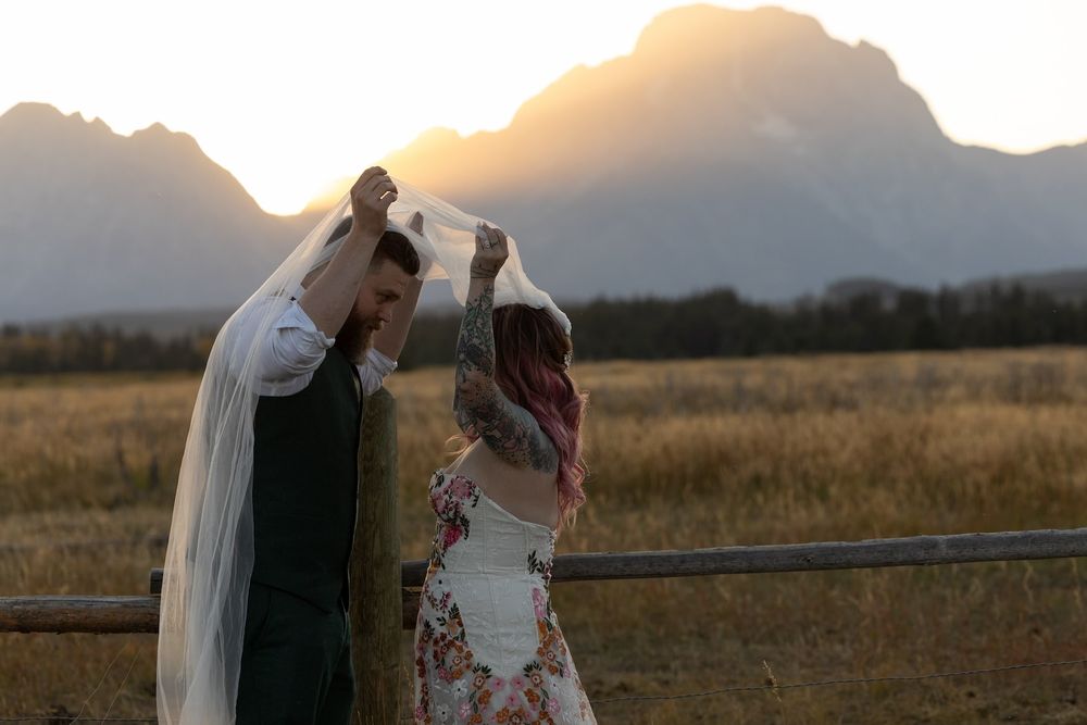Couple embracing in a golden wheat field during sunset with mountains in the background.