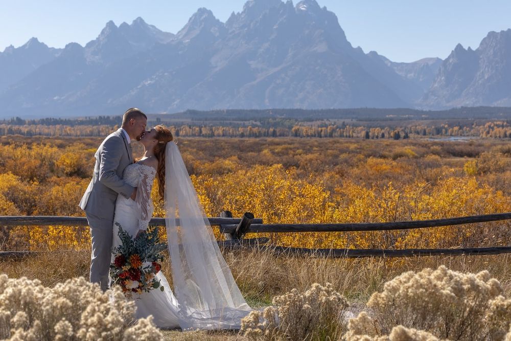 Golden autumn fields stretch toward towering mountain peaks under a bright blue sky.