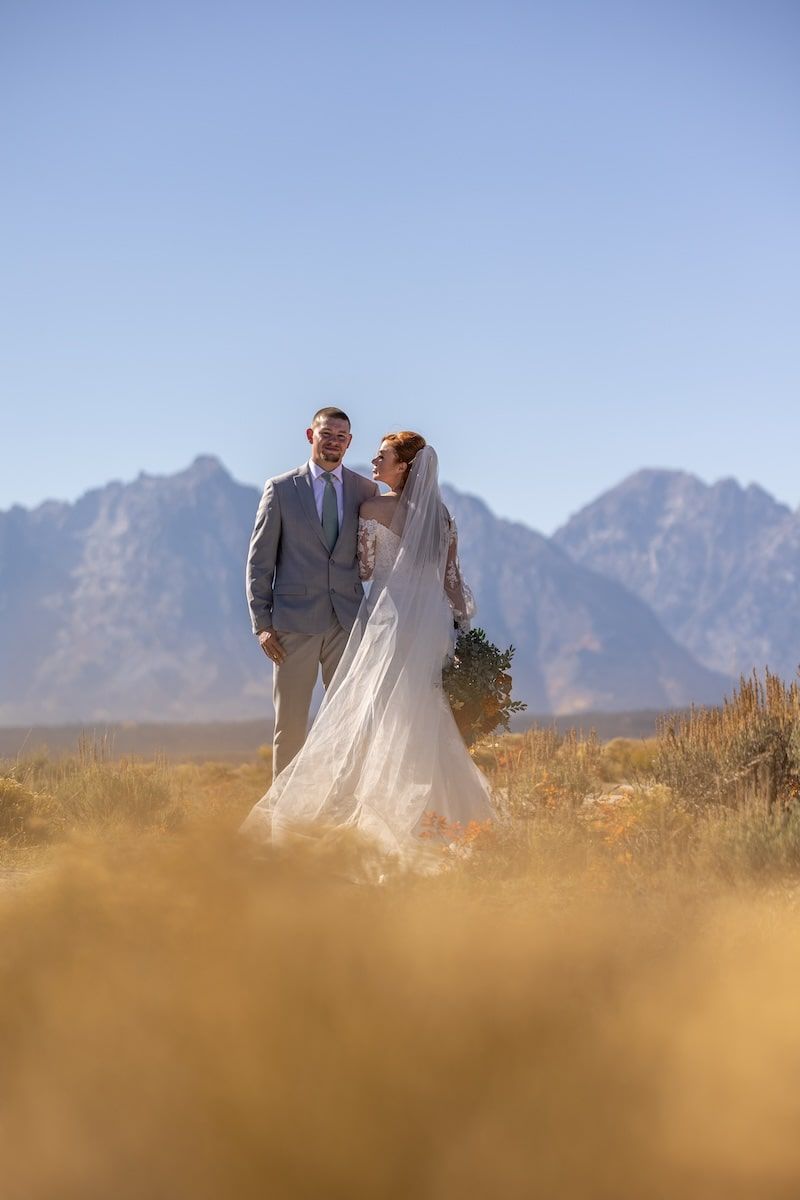 Couple in wedding attire photographed against dramatic mountain landscape with golden grass in foreground.