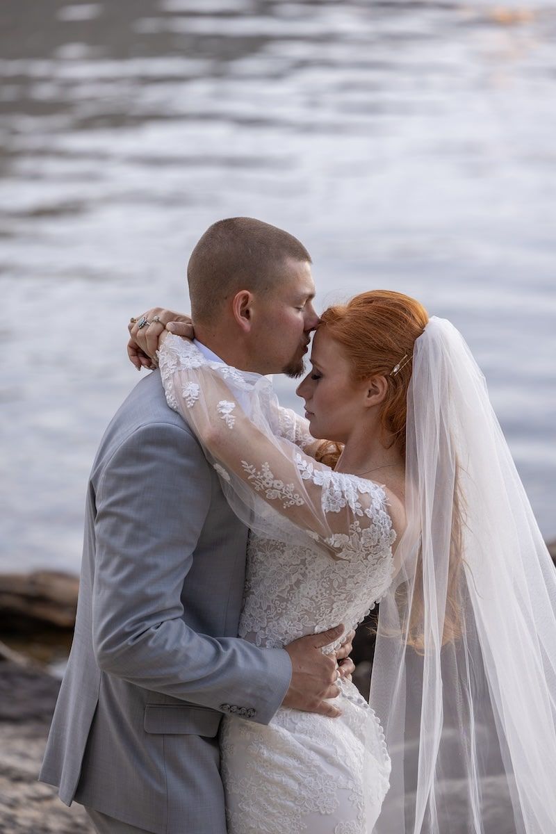 A romantic wedding couple shares tender moments by a waterfront in a series of intimate photographs.