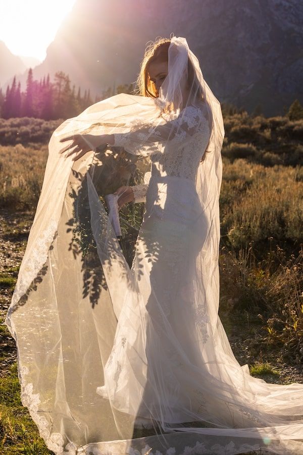 Ethereal wedding dress with flowing sheer fabric billows in the breeze against a mountainous sunset landscape.