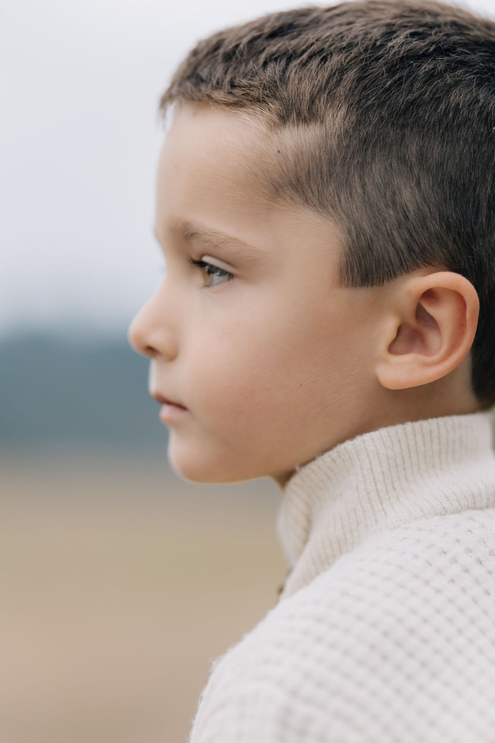 Side profile portrait of a young boy in a cream turtleneck sweater with a thoughtful expression.