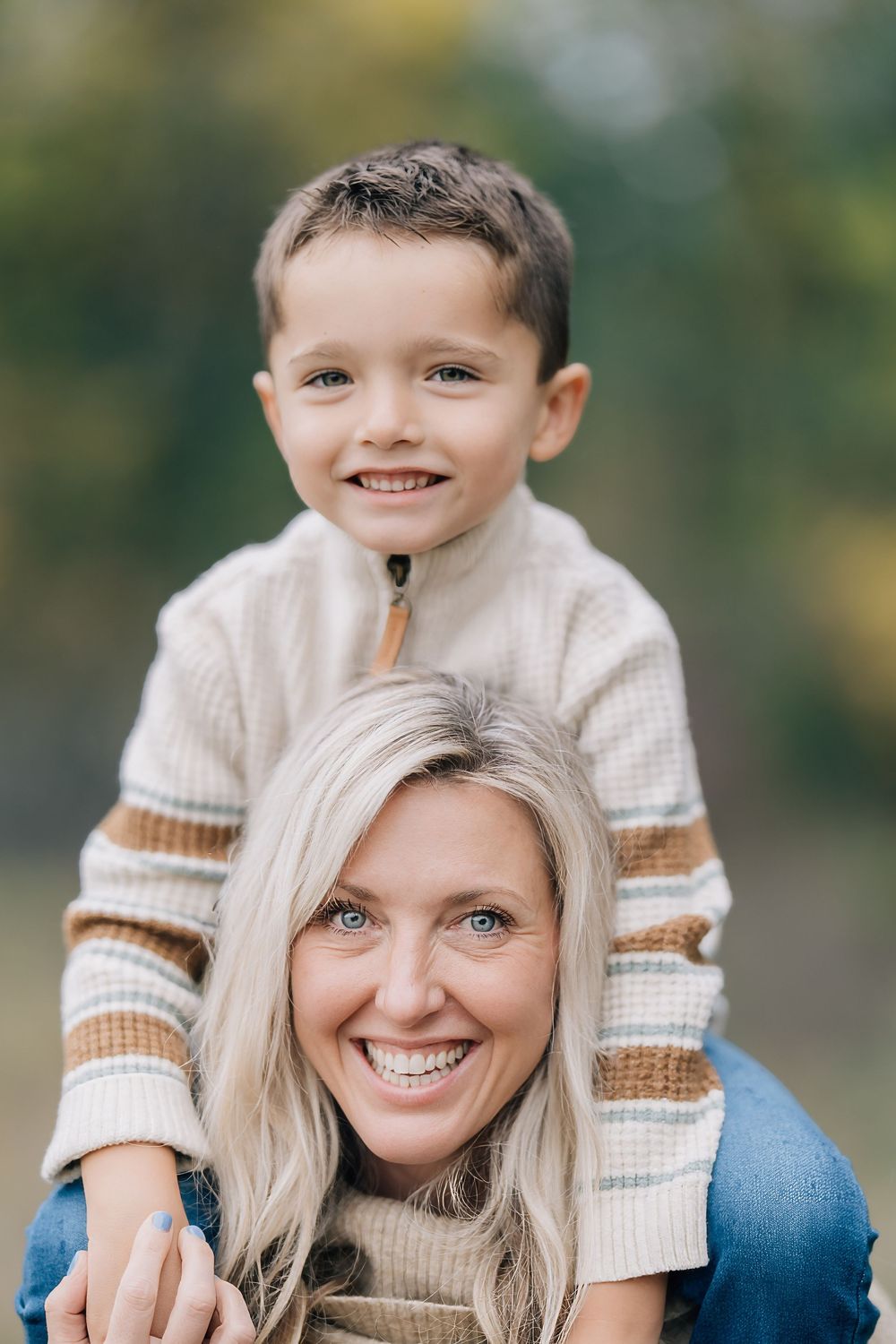 Smiling blonde mother with young boy sitting on her shoulders outdoors in fall.