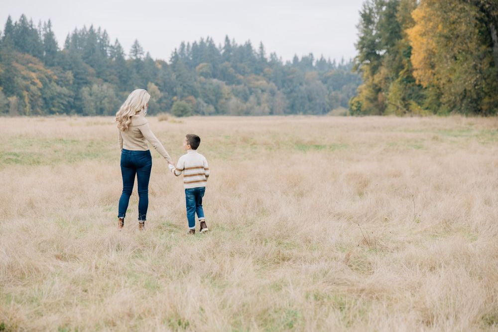 Mother and young son walking hand in hand through a golden autumn meadow.