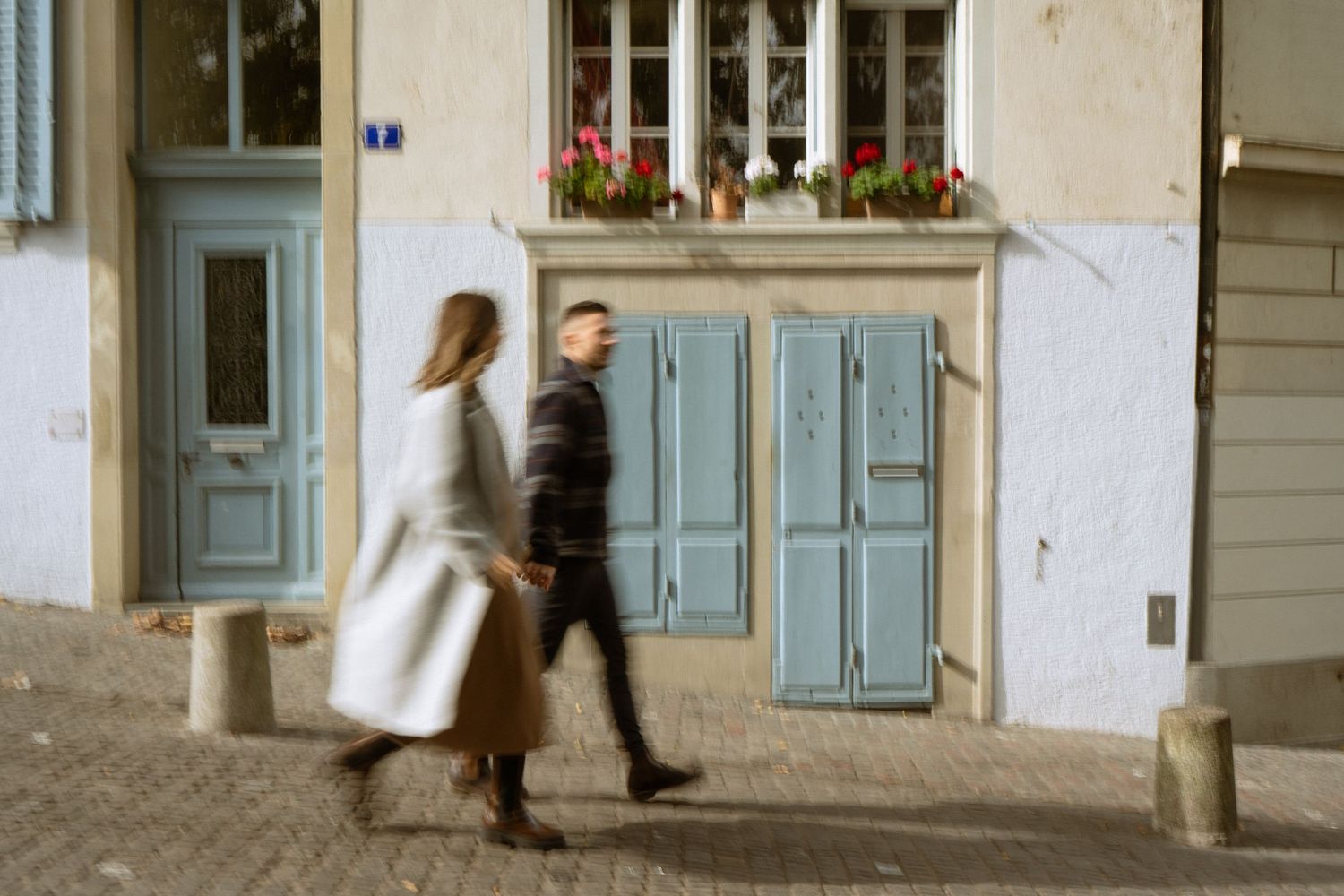 Couple walking past charming European building with blue shutters and flower boxes.