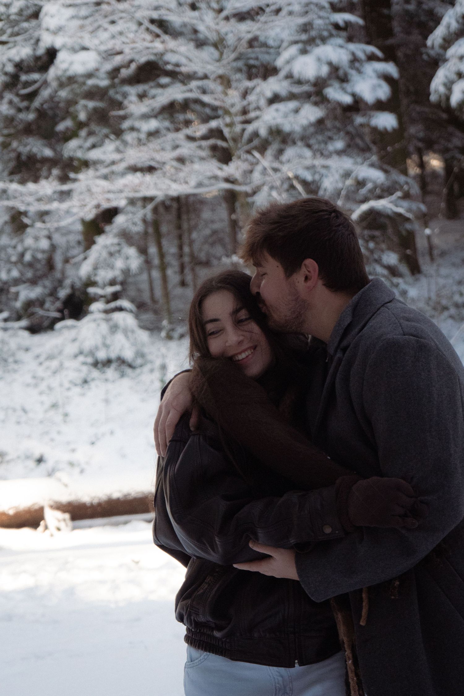 Romantic winter scene with couple embracing in snowy forest setting.