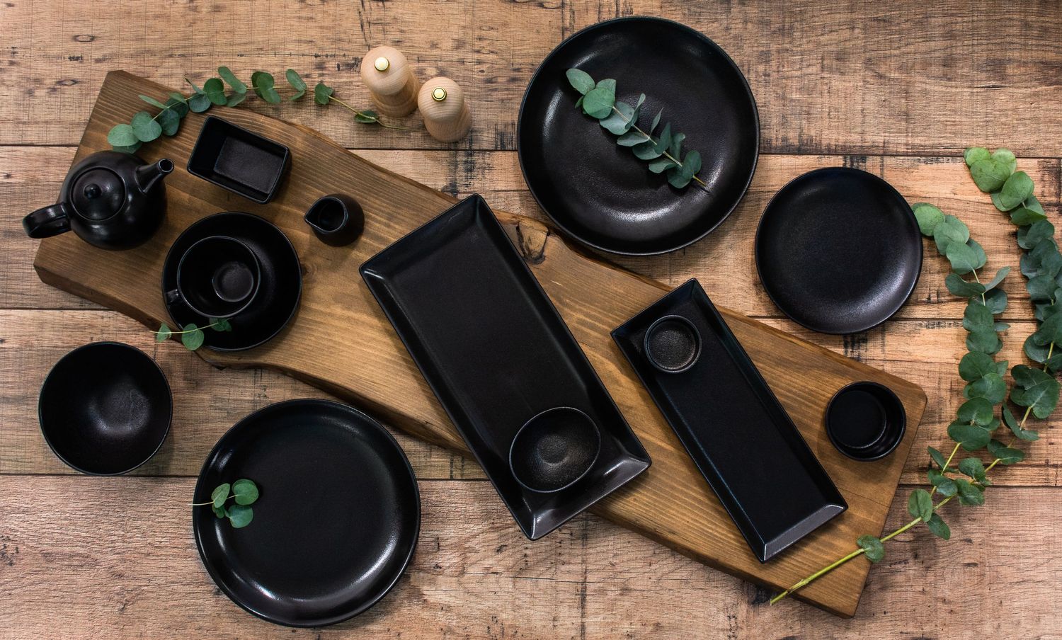 Ceramic kitchenware staged on a wooden board  with eucalyptus leaves and salt and pepper shakers.